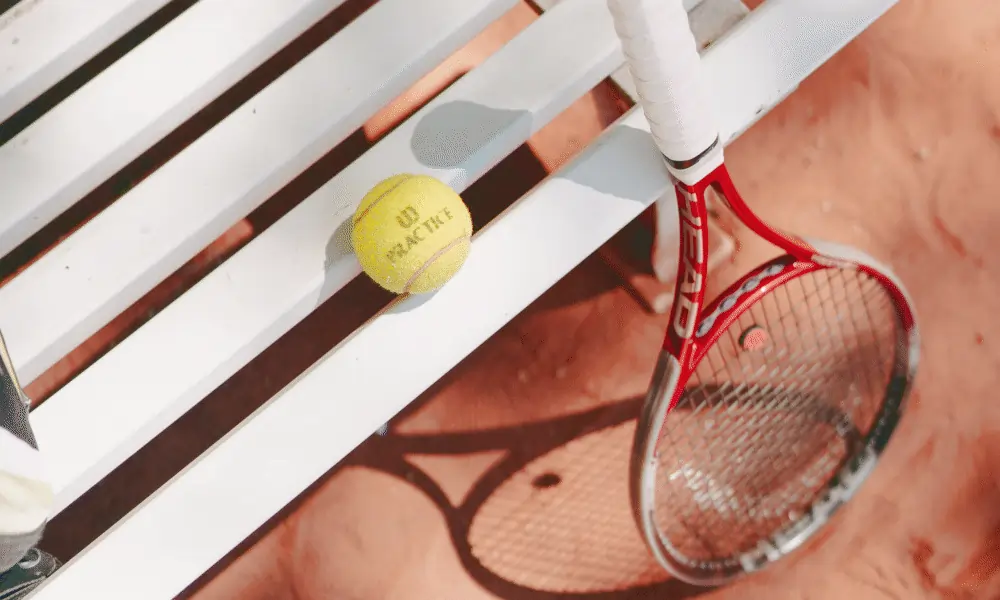 Bild von Tennisschlaeger auf Tennisplatz Sand mit Tennisball auf weisser Bank aus Plastik
